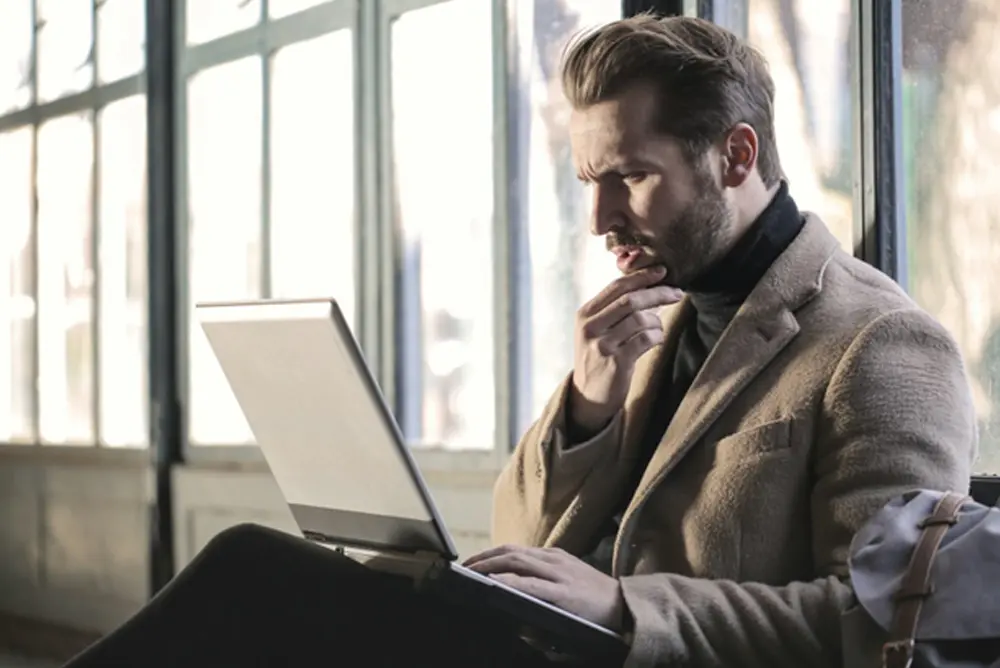 A man with a beard looking at a laptop screen reading