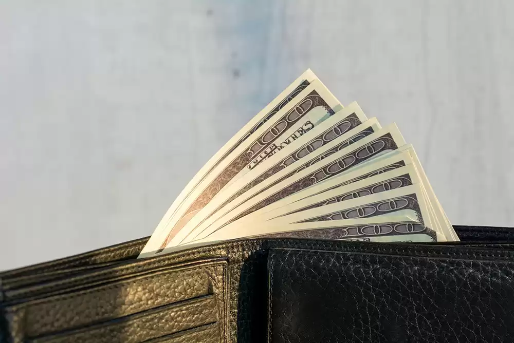 A black leather bifold wallet with ten 100 dollar bills inside