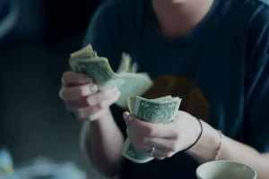 A young woman counting one dollar bills.
